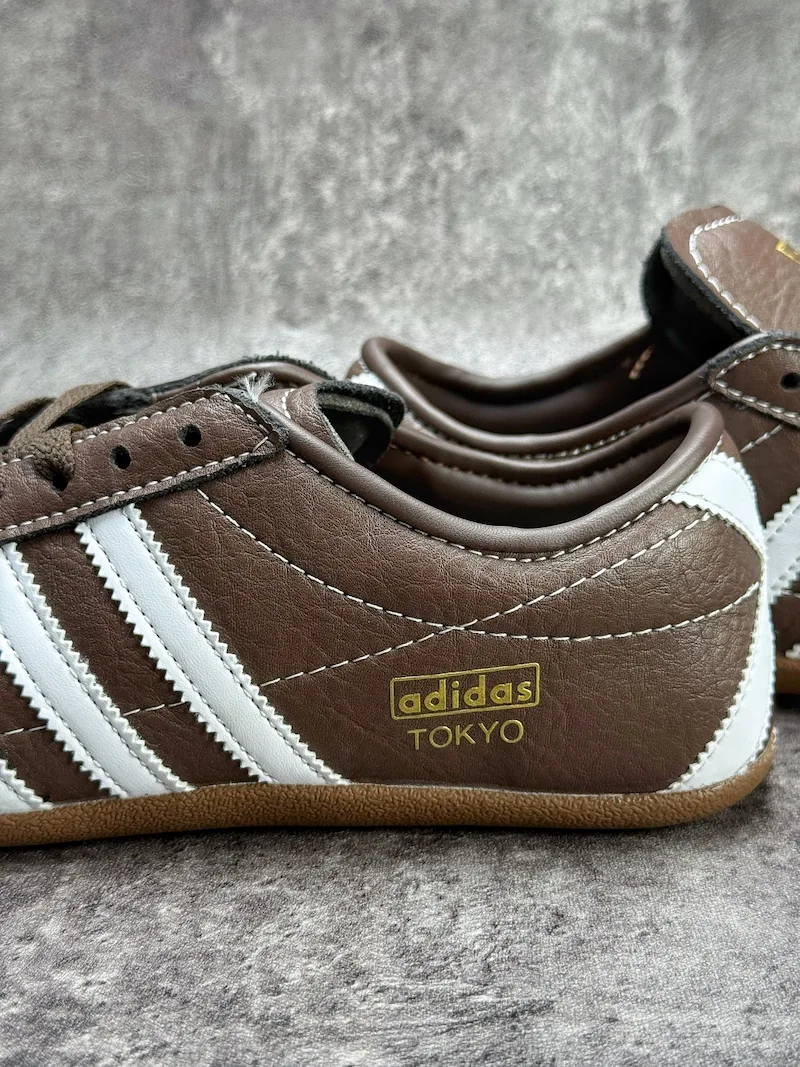 The Adidas Tokyo silhouette originates from the 1964 Tokyo Olympic lightweight track footwear line, positioned as a low-profile retro flat distinct from mass-market Samba OG and Gazelle. This full brown leather reissue launched late 2025, optimized for year-round lifestyle retail use. Compared to canvas vintage versions, grained cowhide improves durability and wear-in texture; the slim elongated last and thin gum sole create a slimmer foot silhouette without bulky padding.