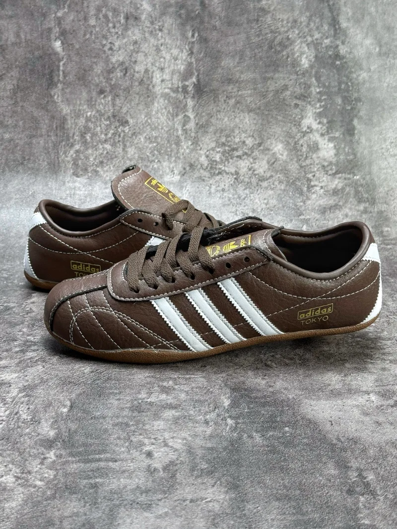 The Adidas Tokyo silhouette originates from the 1964 Tokyo Olympic lightweight track footwear line, positioned as a low-profile retro flat distinct from mass-market Samba OG and Gazelle. This full brown leather reissue launched late 2025, optimized for year-round lifestyle retail use. Compared to canvas vintage versions, grained cowhide improves durability and wear-in texture; the slim elongated last and thin gum sole create a slimmer foot silhouette without bulky padding.