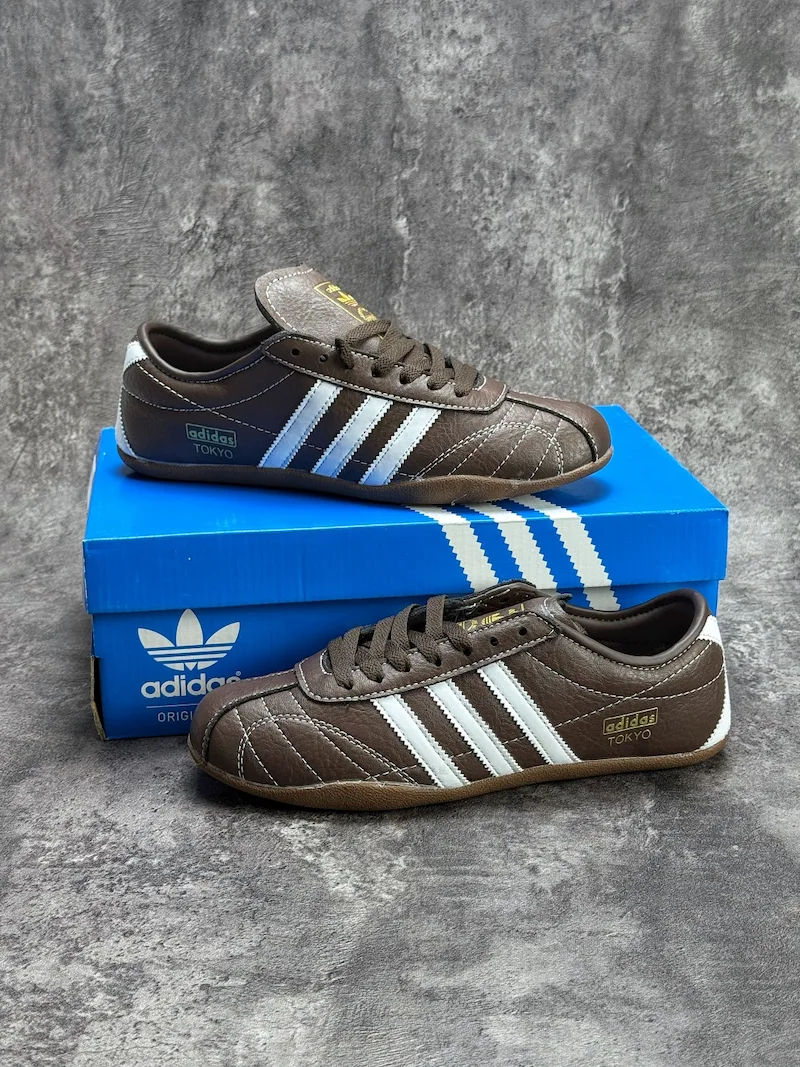 The Adidas Tokyo silhouette originates from the 1964 Tokyo Olympic lightweight track footwear line, positioned as a low-profile retro flat distinct from mass-market Samba OG and Gazelle. This full brown leather reissue launched late 2025, optimized for year-round lifestyle retail use. Compared to canvas vintage versions, grained cowhide improves durability and wear-in texture; the slim elongated last and thin gum sole create a slimmer foot silhouette without bulky padding.
