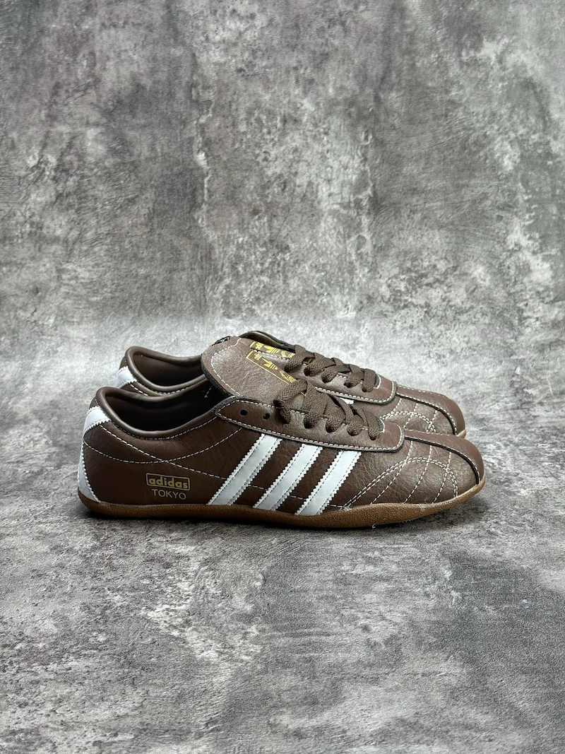 The Adidas Tokyo silhouette originates from the 1964 Tokyo Olympic lightweight track footwear line, positioned as a low-profile retro flat distinct from mass-market Samba OG and Gazelle. This full brown leather reissue launched late 2025, optimized for year-round lifestyle retail use. Compared to canvas vintage versions, grained cowhide improves durability and wear-in texture; the slim elongated last and thin gum sole create a slimmer foot silhouette without bulky padding.