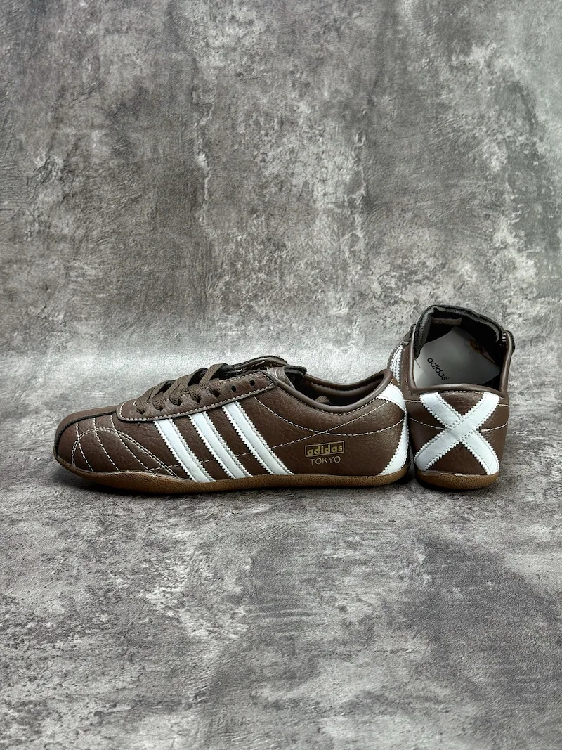 The Adidas Tokyo silhouette originates from the 1964 Tokyo Olympic lightweight track footwear line, positioned as a low-profile retro flat distinct from mass-market Samba OG and Gazelle. This full brown leather reissue launched late 2025, optimized for year-round lifestyle retail use. Compared to canvas vintage versions, grained cowhide improves durability and wear-in texture; the slim elongated last and thin gum sole create a slimmer foot silhouette without bulky padding.